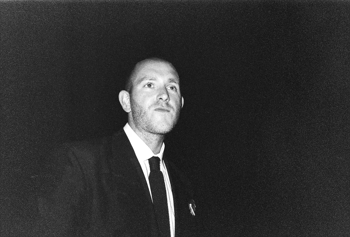 Portrait of Yiğit Özen in a dark suit and tie, photographed against black.